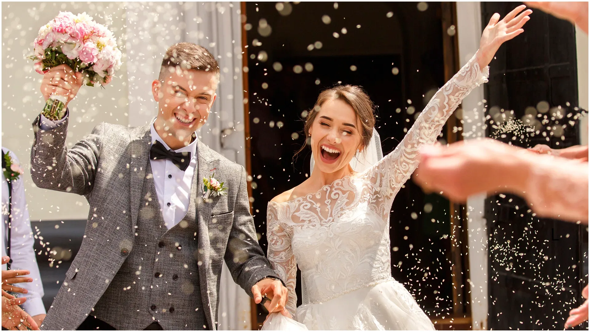 Newlywed bride and groom celebrating outside a church as guests shower them with confetti.