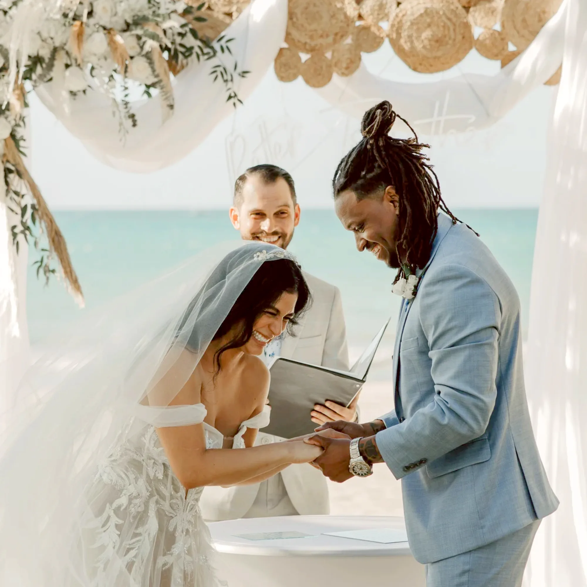 Bride and groom laughing together while exchanging wedding vows during a beach wedding ceremony.